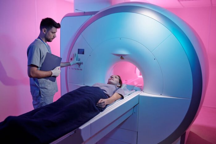 Młody lekarz w uniformie naciskający przycisk start maszyny do rezonansu magnetycznego z pacjentem leżącym na długim stole